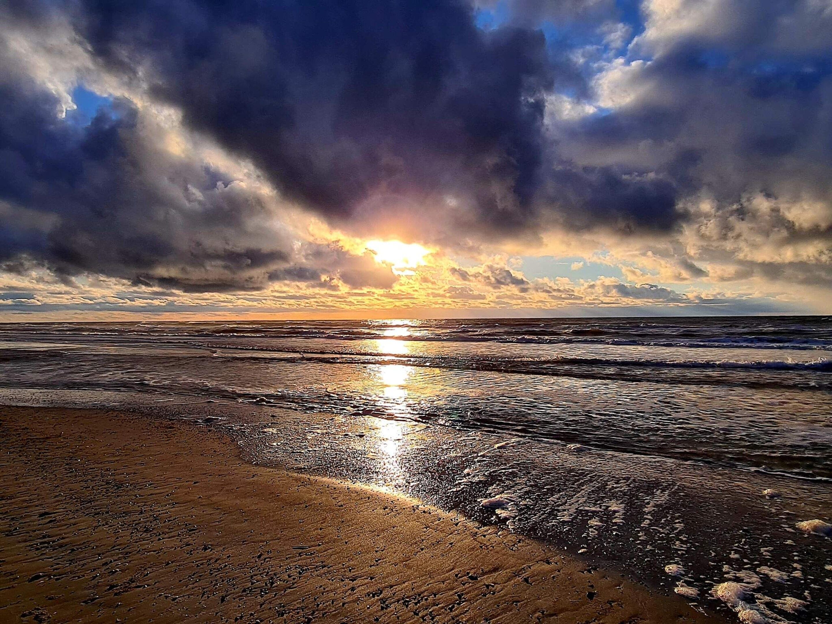 A beach with waves and a sunset.