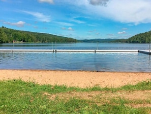 Un lac avec une rive sablonneuse et une zone herbeuse au premier plan.