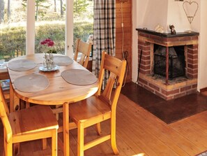 Une table de salle à manger en bois, agrémentée de sets de table, de chaises, d’une cheminée et offrant une vue sur l’extérieur.