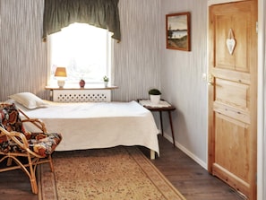A bedroom with a bed, a chair, a window with curtains, a bedside table with a lamp, and a door. - 5 Person Holiday Home in Fengersfors (Fengersfors)