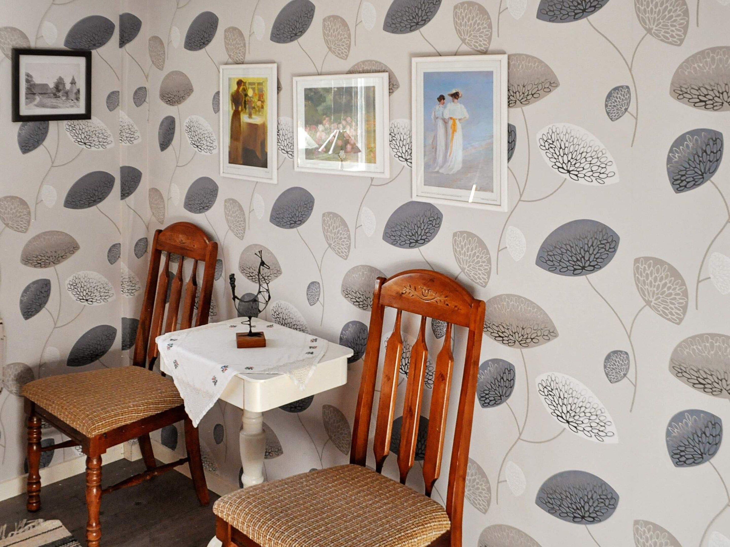 A dining area with two wooden chairs, a small table, and a wall decorated with leaf patterns and framed pictures.