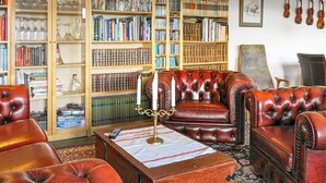 Eine Bibliothek mit Ledersesseln, Bücherregalen und einem antiken Schreibtisch mit Kerzenleuchter.
