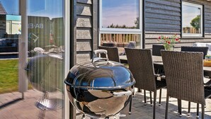 An outdoor patio with a Weber grill, wicker chairs, and a view of the backyard. - Holiday Home in Kappeln (Kappeln)