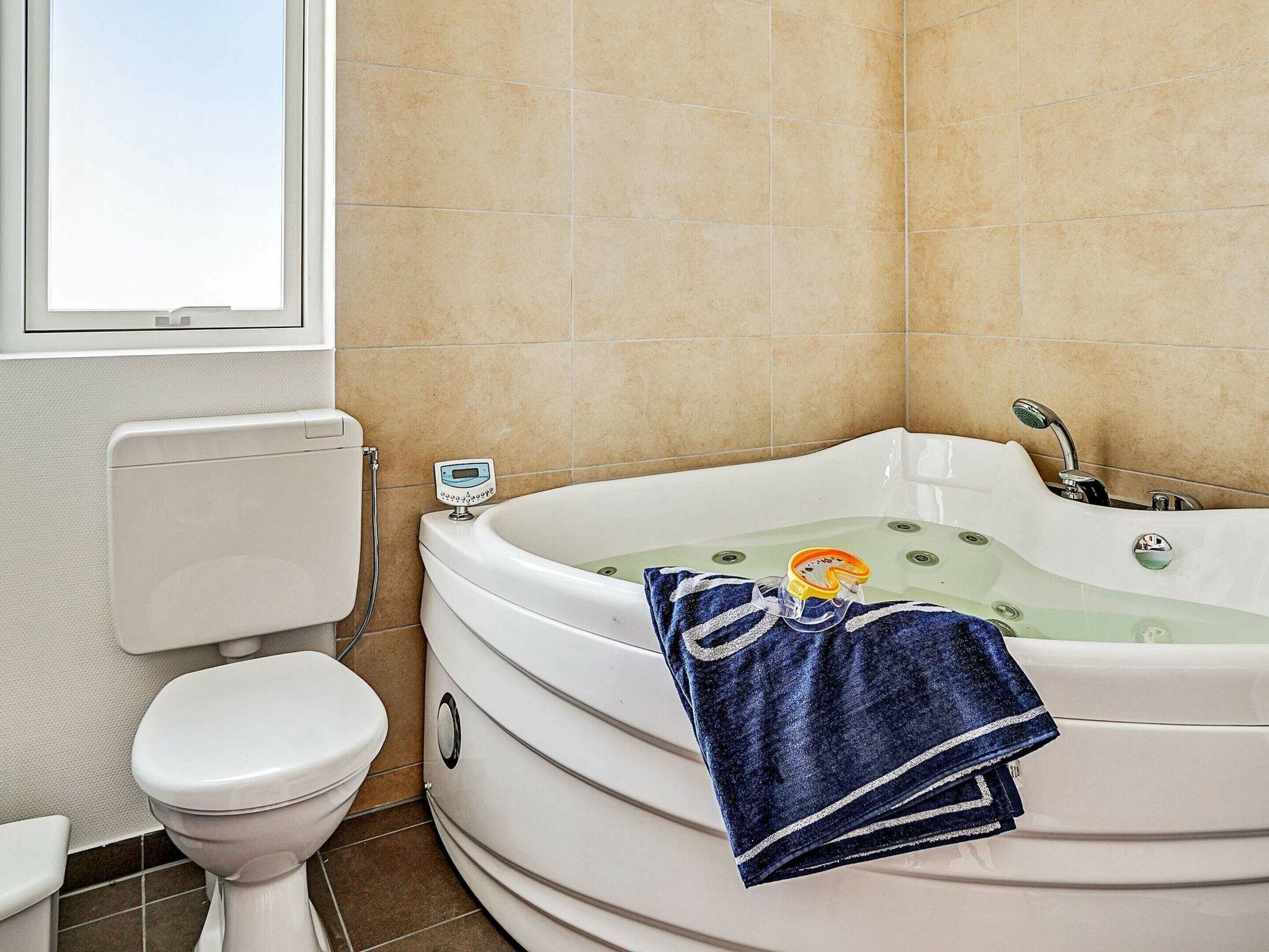A bathroom with a white toilet, a bathtub with a digital thermometer, and a towel on the edge of the tub.
