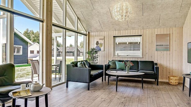 A spacious living area with large windows, a wooden ceiling, and a cozy seating arrangement including a sofa and a chair. - Holiday Home in Kappeln (Kappeln)