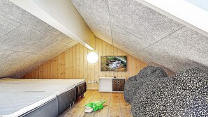 A cozy attic bedroom with a sloped ceiling, a bed, a small dresser, a leopard-print pouf, and a TV on the wall. - Holiday Home in Kappeln (Kappeln)