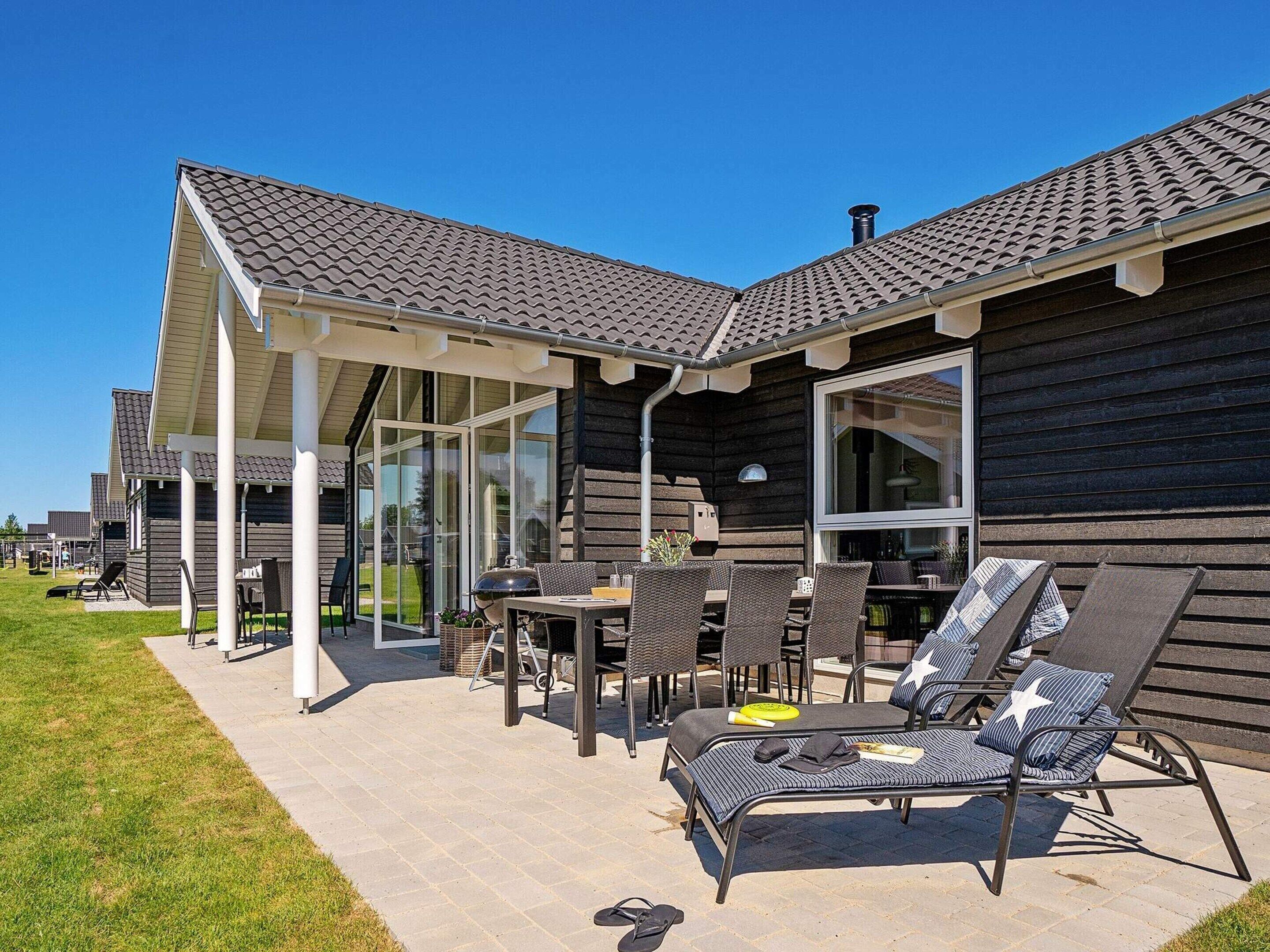 En træbygning med en overdækket terrasse, udendørs møbler og en grill.