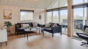 A modern living room with a sofa set, a coffee table, and large windows offering a view of the outdoors. - Holiday Home in Kappeln (Kappeln)