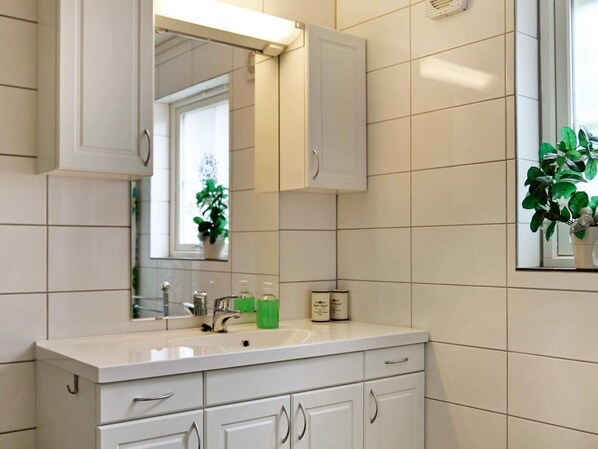 Une salle de bain avec des carreaux blancs, un lavabo, un miroir et des placards.