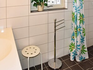 Ein Badezimmer mit weißen Fliesen, einem kleinen Hocker, einem Handtuchhalter, einer Topfpflanze und einem Duschvorhang mit Blumenmuster.