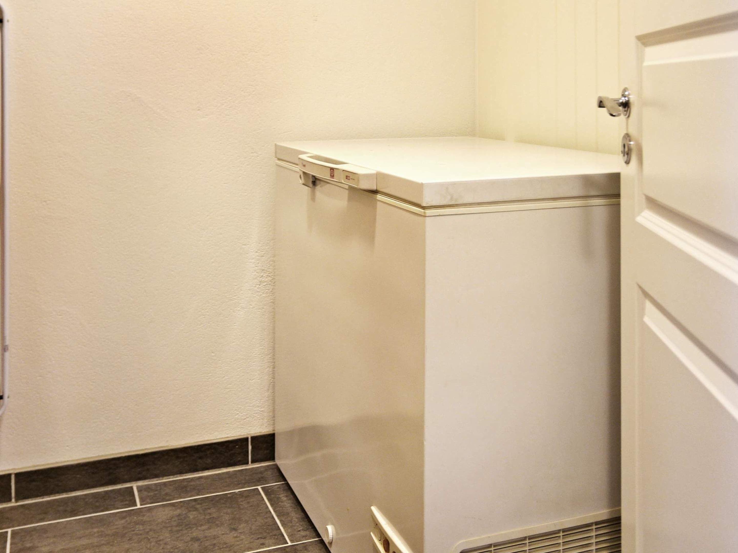 Um espaço pequeno e funcional, com piso ladrilhado, aquecedor e porta com puxador prateado.