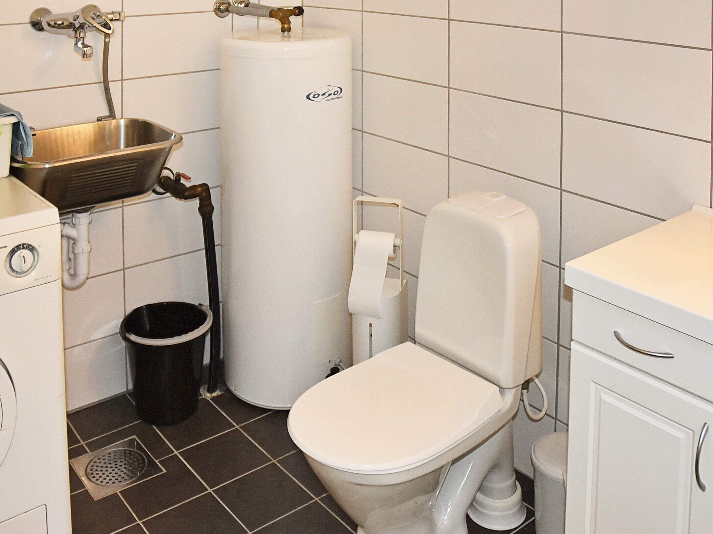 A bathroom with a toilet, a sink, a water heater, and a trash bin.