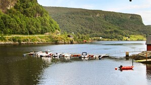 Un lac paisible où sont amarrés des bateaux, entouré de collines boisées et d’un petit bâtiment.