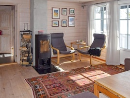 Una sala de estar acogedora con una chimenea de leña, dos sillones, una mesita pequeña y una alfombra colorida.