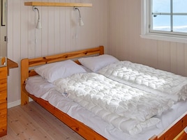Una cama de madera con ropa de cama blanca, una mesita de noche de madera y una ventana con vistas al exterior.