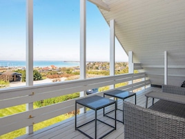 A balcony with a view of the sea, a covered area with tables and chairs, and a white railing.