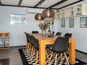 A dining area with a wooden table, black chairs, a checkered rug, a vase with flowers, and wall-mounted shelves with glassware.