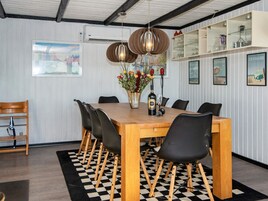 A dining area with a wooden table, black chairs, a checkered rug, a vase with flowers, and wall-mounted shelves with glassware.