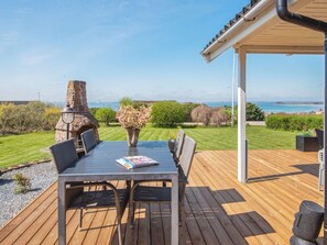An outdoor patio with a table and chairs, a stone fireplace, and a view of the sea. - Fantastic Holiday Home with Bay View near Knebel (Knebel)
