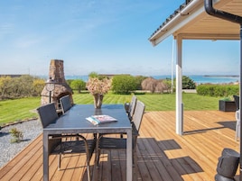 Un patio exterior con una mesa, sillas, una chimenea de piedra y vistas al mar.