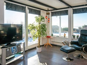 A modern living room with a TV, a potted plant, a leather chair, and large windows with a view.
