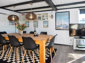 A dining area with a wooden table, black chairs, a vase of flowers, a bottle of wine, and a television on a stand.