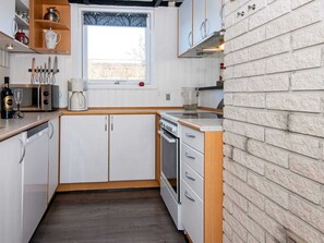 Une cuisine compacte avec des meubles blancs, un four encastré, un four à micro-ondes et une fenêtre donnant sur l’extérieur.