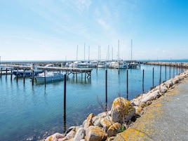A marina with boats docked at wooden piers, a rocky shoreline, and a clear sky.