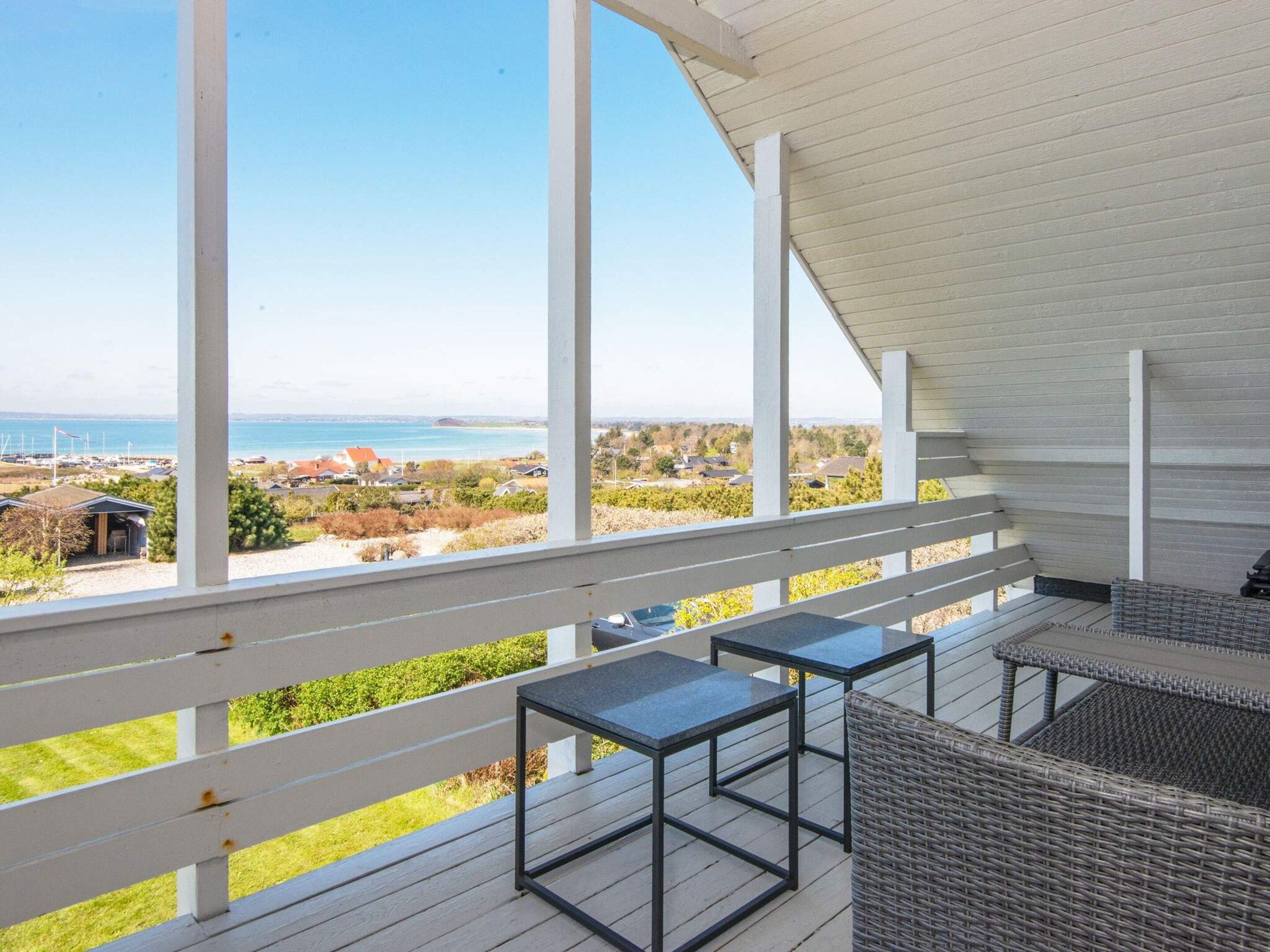 Área externa coberta com vista para o mar, com uma mesa e cadeiras.