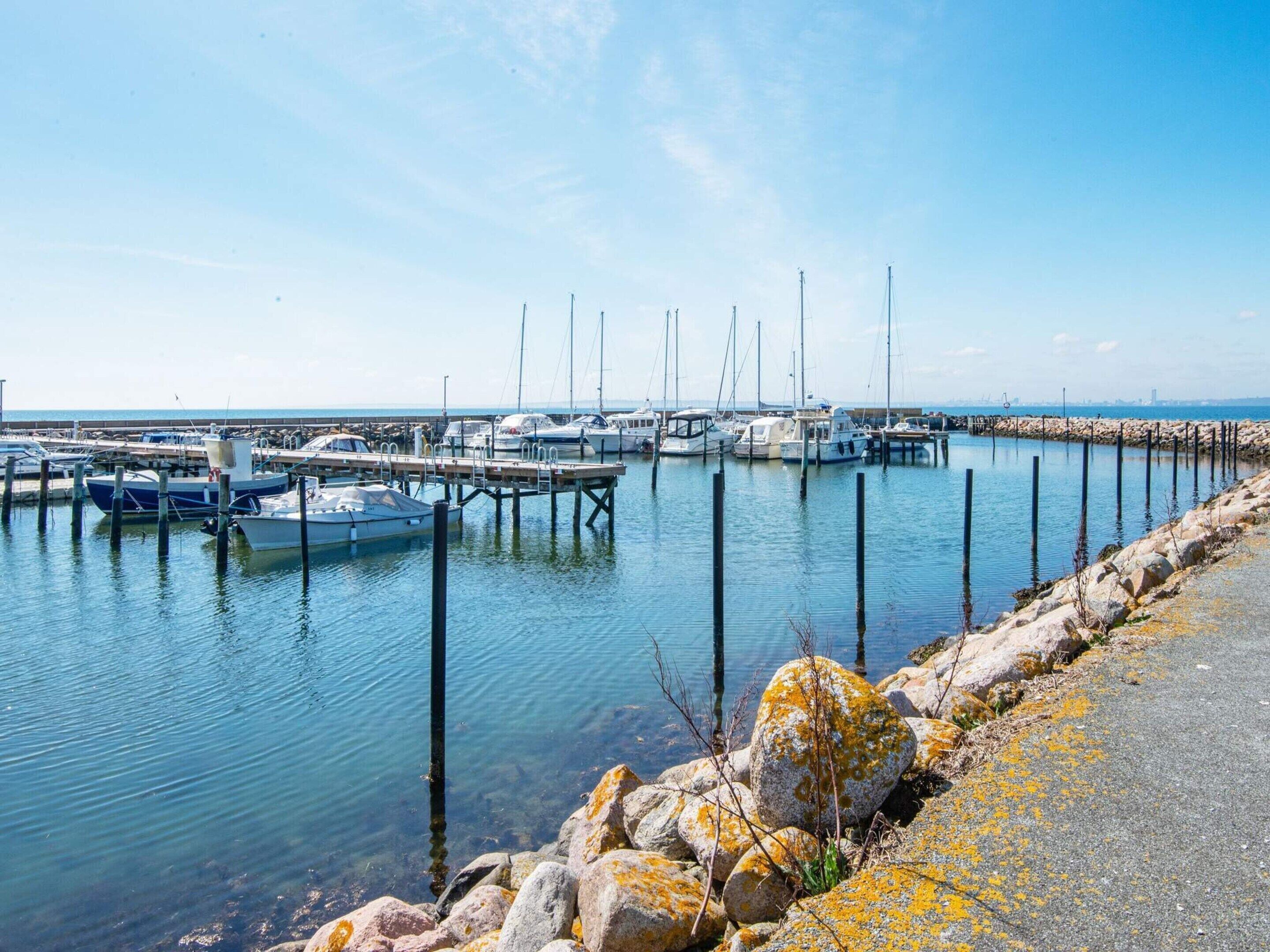 A marina with boats docked, a rocky shoreline, and a clear sky.