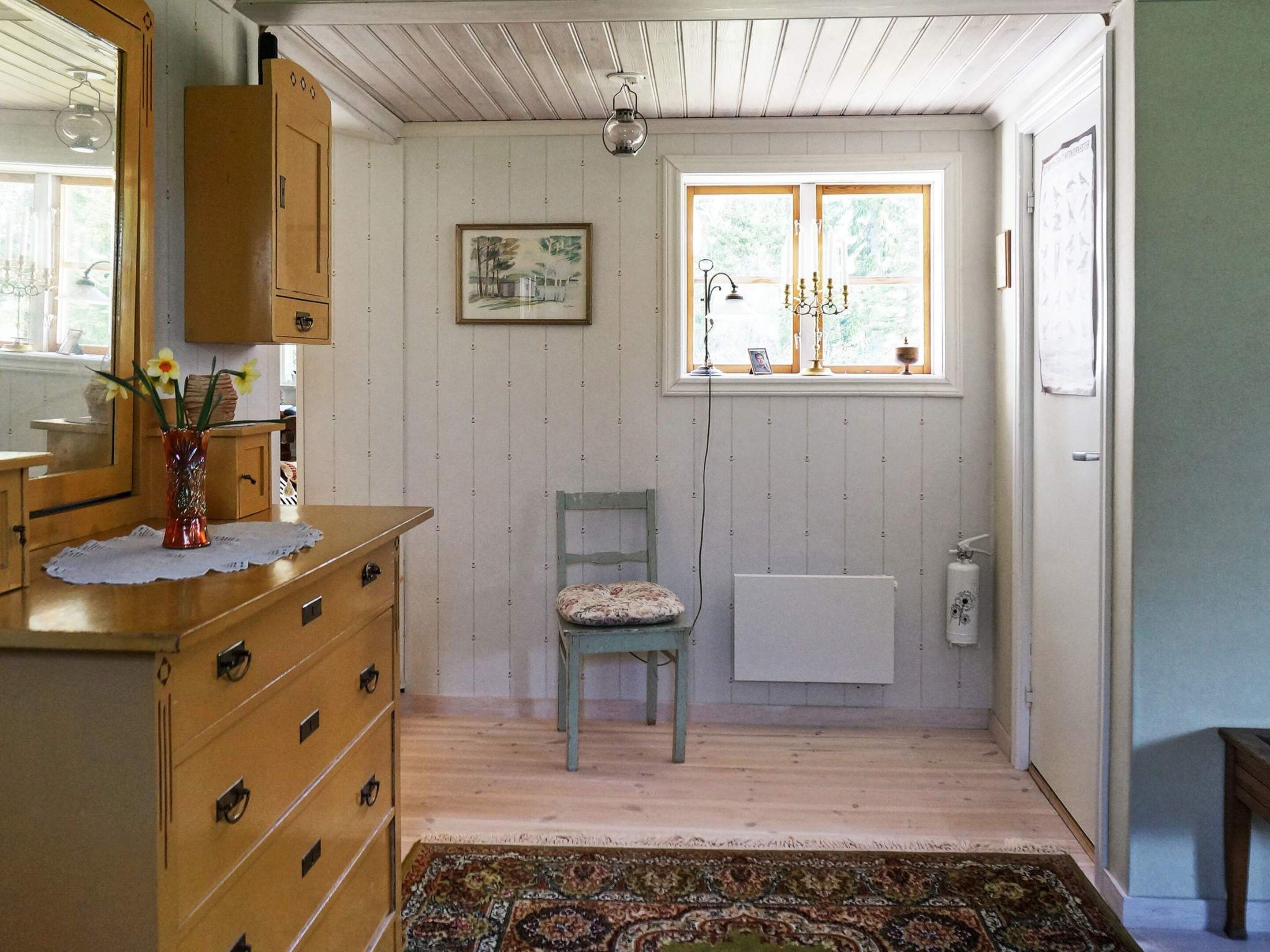 Una habitación con un aparador de madera, una silla, un radiador y una ventana con vistas a zonas verdes.