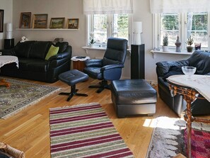 A living room with a black leather sofa, a blue armchair, a wooden coffee table, and a patterned rug. - 5 Person Holiday Home in Kristinehamn (Kristinehamn)
