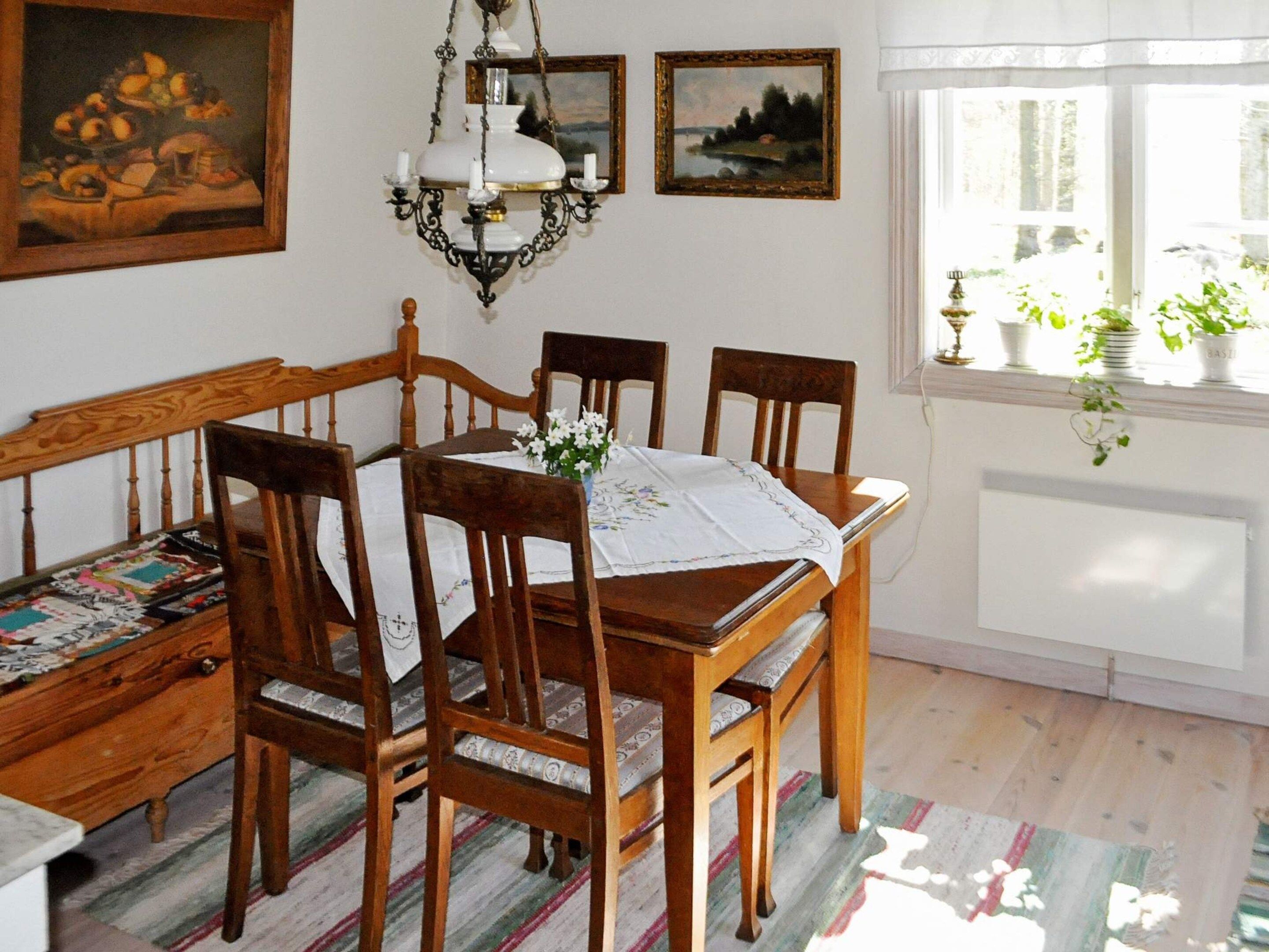 A dining room with a wooden table, four chairs, a chandelier, and a window with plants.