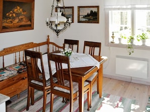 A dining room with a wooden table, four chairs, a chandelier, and a window with plants.