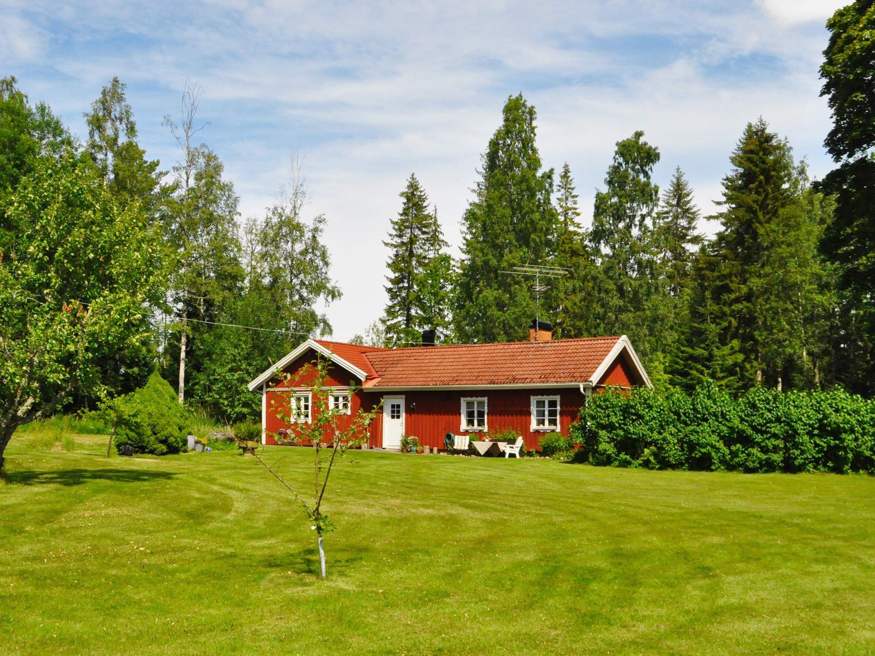 A red house with a red roof, surrounded by a well-maintained lawn and dense trees.