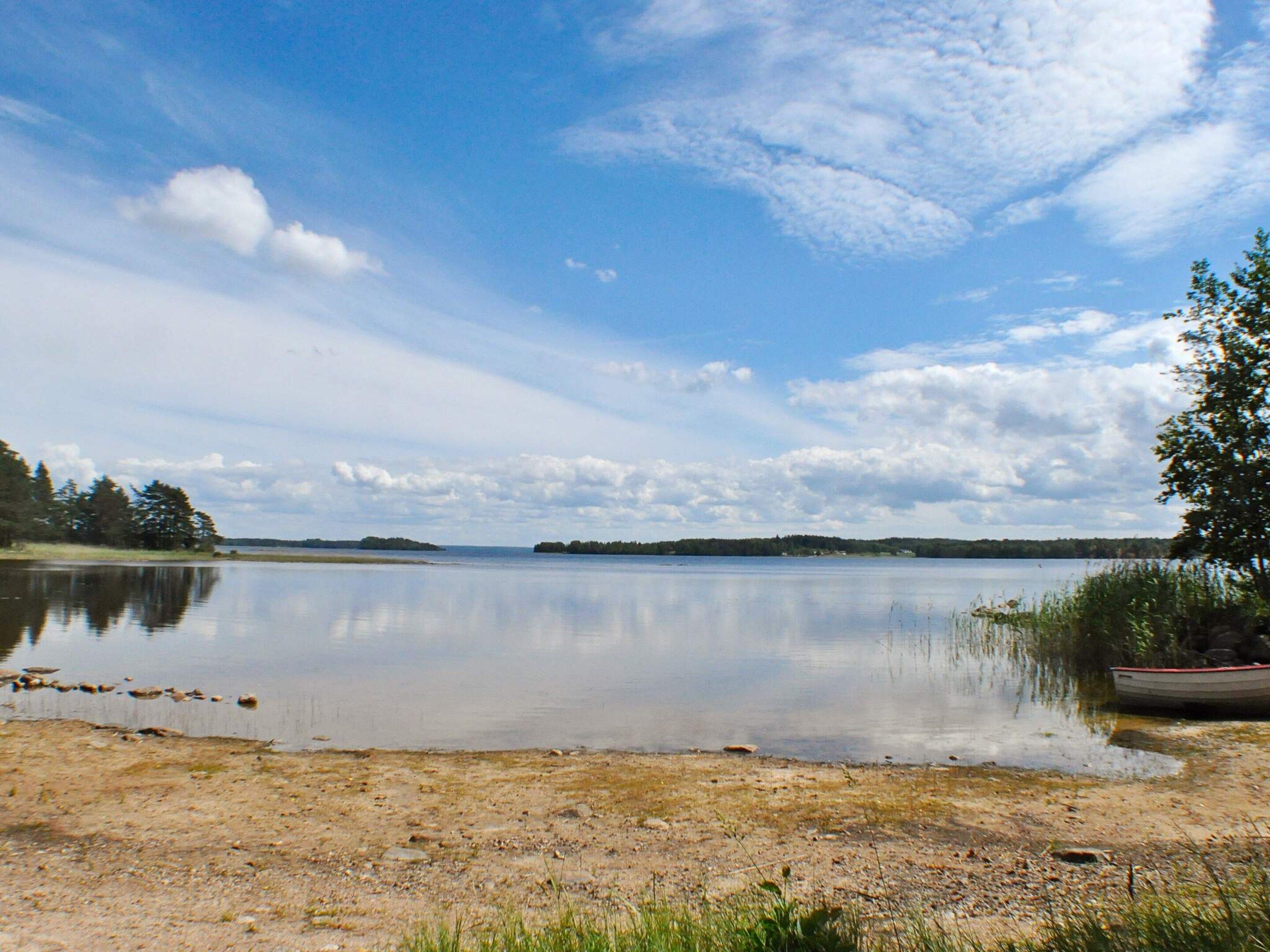 A calm lake with a boat on the right, surrounded by trees and a clear sky.