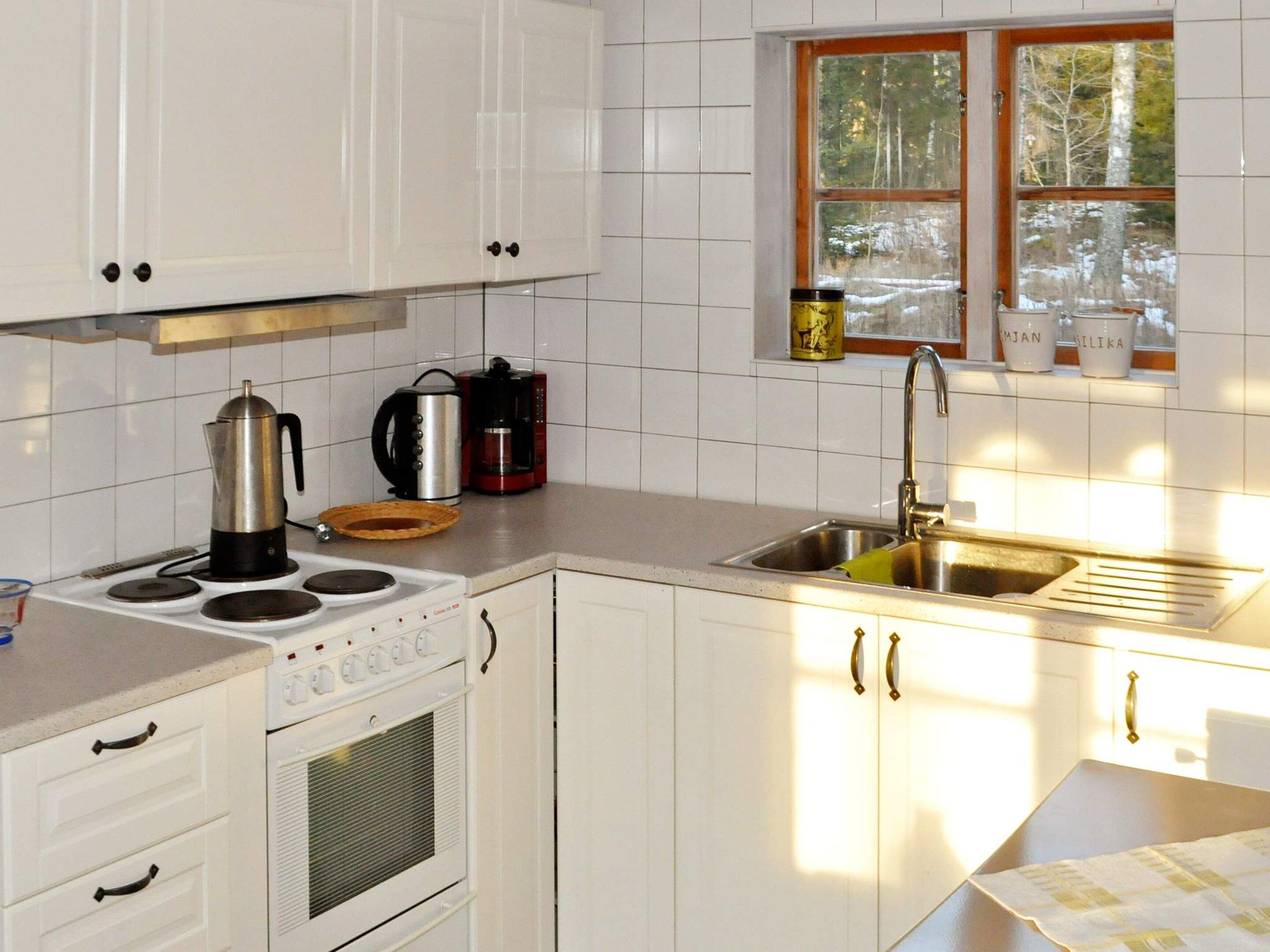 A kitchen with white cabinets, a stove, a sink, and a window with a view of trees.