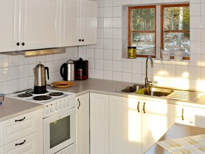 A kitchen with white cabinets, a stove, a sink, and a window with a view of trees. - 5 Person Holiday Home in Kristinehamn (Kristinehamn)