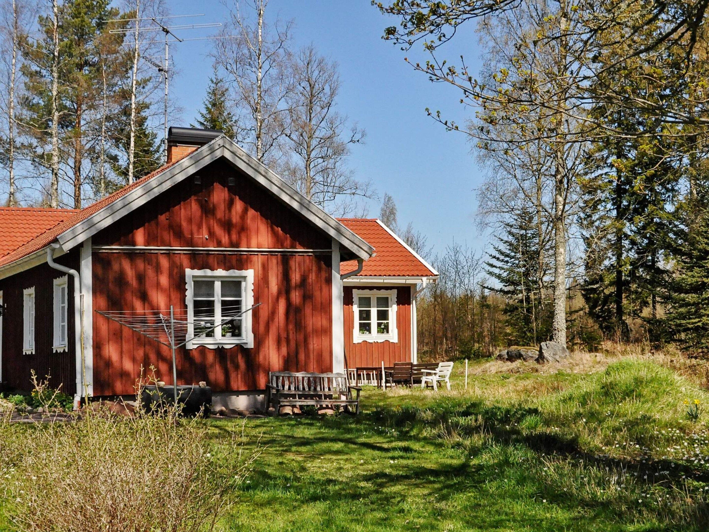 A red wooden cabin with a sloped roof, a small porch with a bench, and a clothesline.