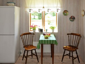 A room with a white refrigerator, a table with a green tablecloth, two wooden chairs, and a window with a view of greenery. - 5 Person Holiday Home in Kristinehamn (Kristinehamn)