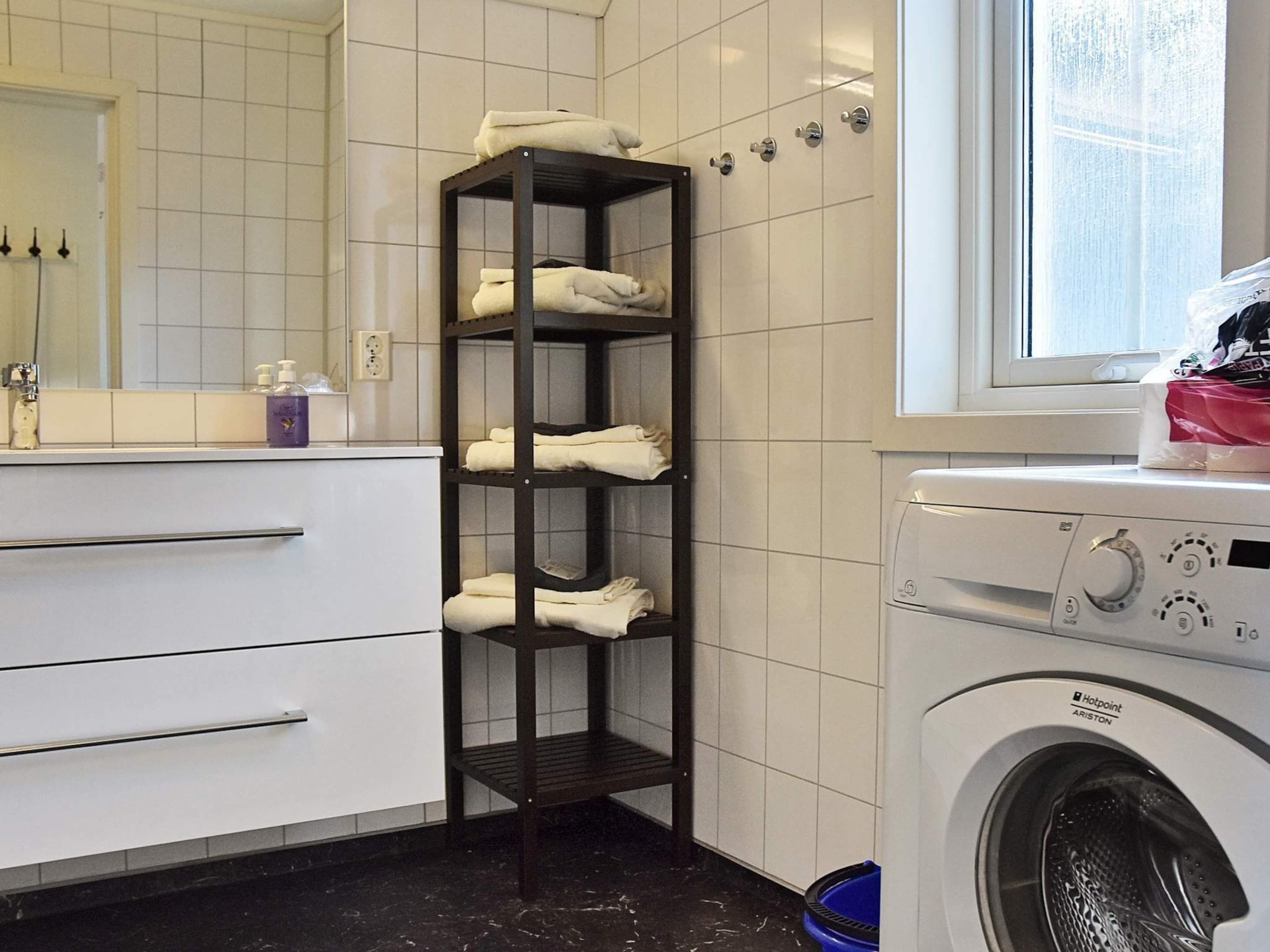 A laundry area with a washing machine, a towel rack, and a tiled wall.