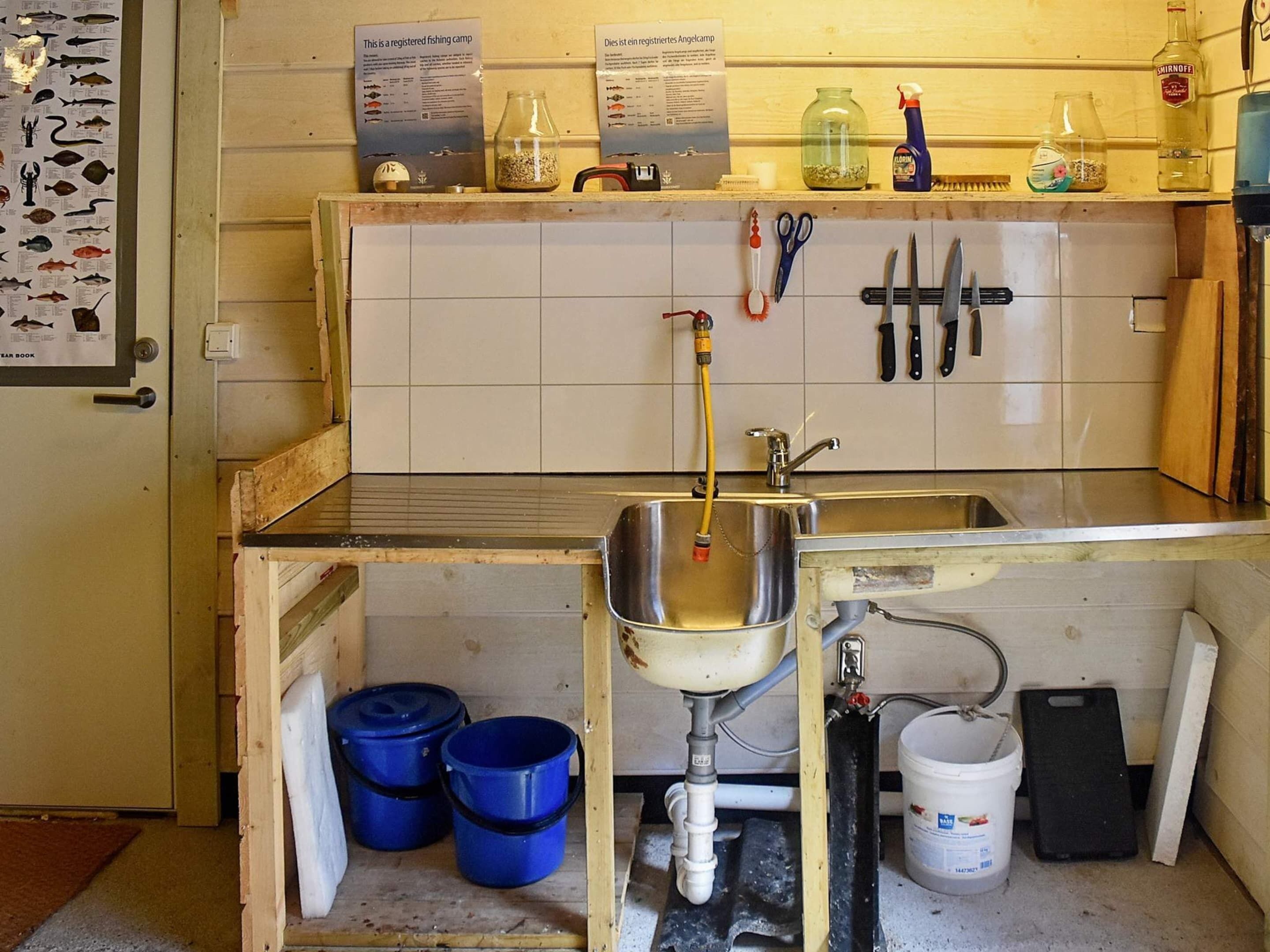 A kitchen with a sink, blue buckets, a white bucket, and various kitchen tools.