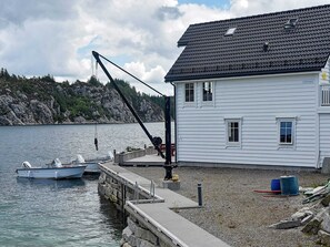 Une maison avec une jetée qui s’avance dans une eau calme, un bateau amarré à la jetée et une côte rocheuse en arrière-plan.