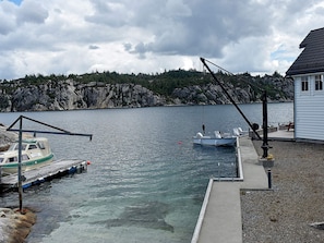 Un quai avec des bateaux, un petit bâtiment et une côte rocheuse bordée d’arbres.