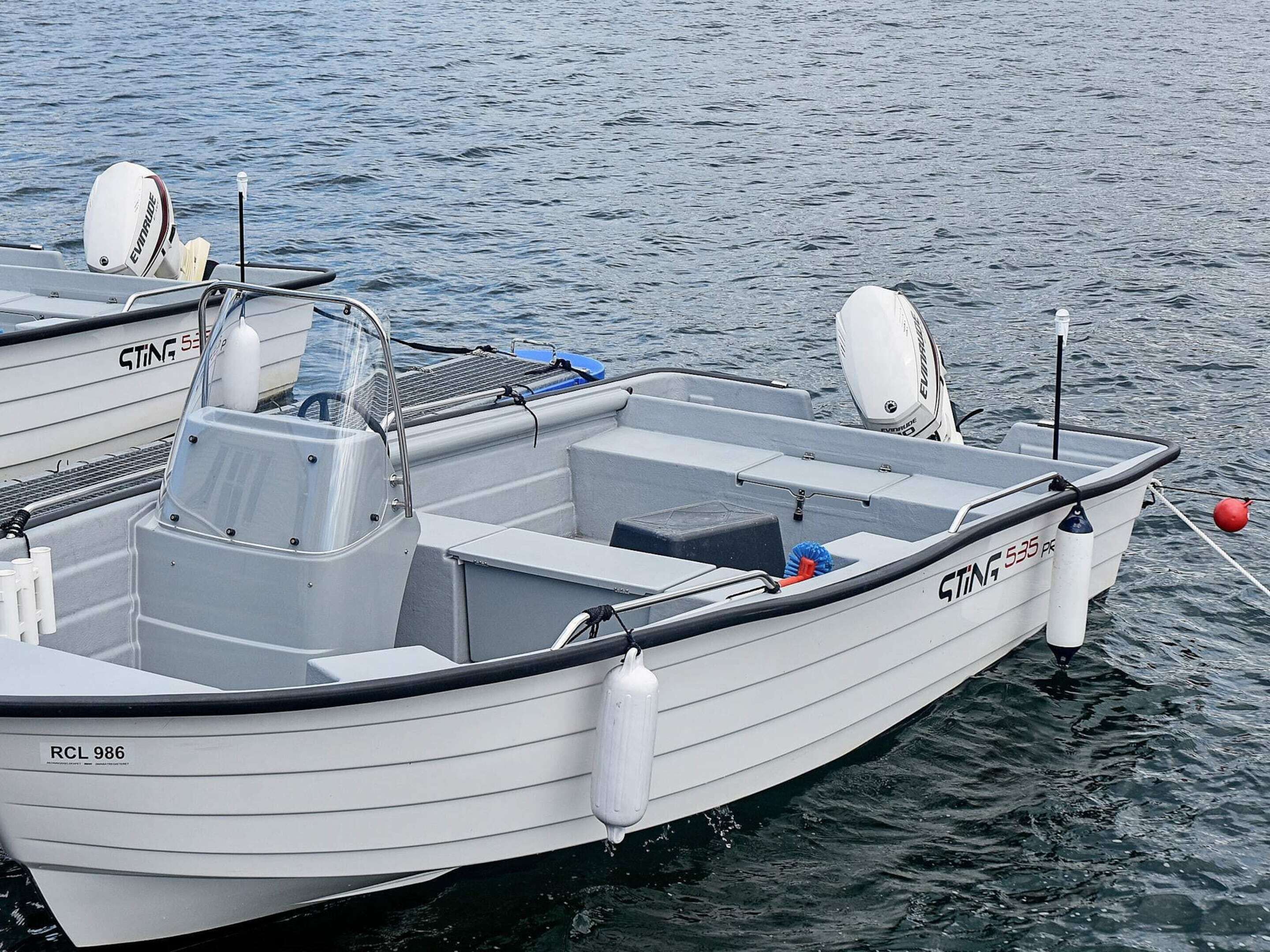A small, white motorboat named 'STING 535' docked at a marina.