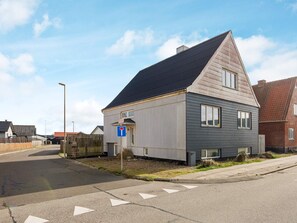 A two-story residential building with a dark roof and light siding, a visible garage door, and a street in front.