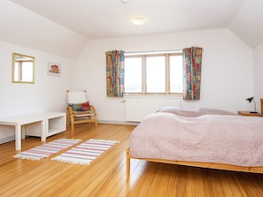 A bedroom with a bed, a chair, a desk, and a window with curtains.