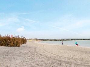 Une plage de sable avec une digue rocheuse, un ciel dégagé et une mer calme.
