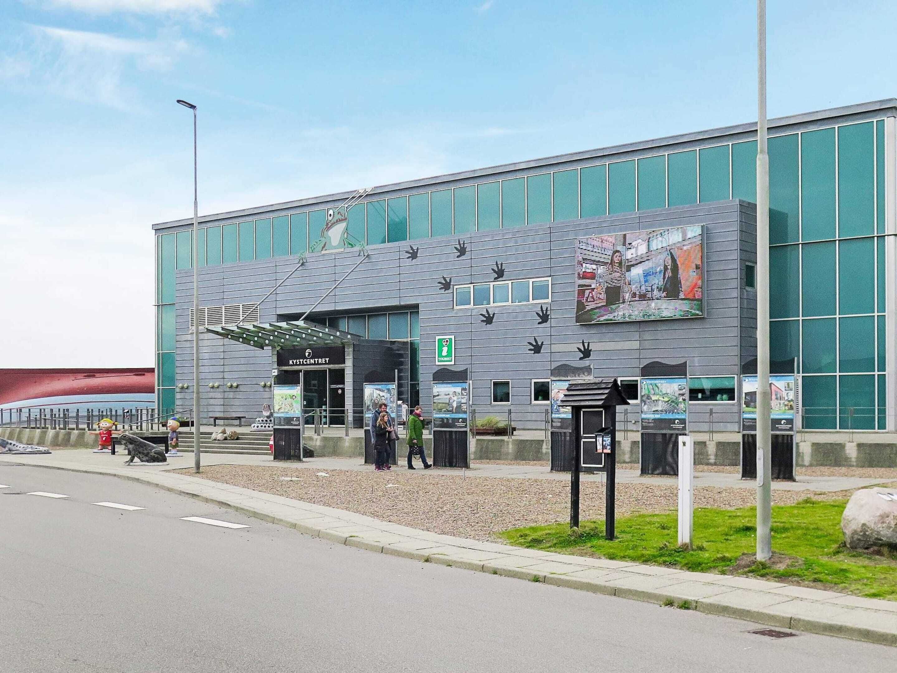 A modern building with a glass facade, a prominent sign reading "KYSTCENTRE", and a large digital display on the side.