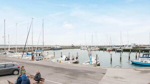 A marina with boats docked, a road with a car, and people sitting on benches. - 8 Person Holiday Home in Thyboron-by Traum (Thyborøn)